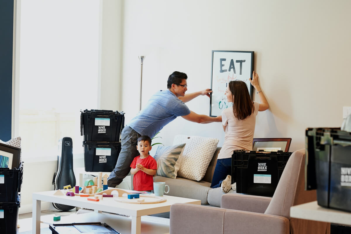 People hanging a picture on the wall in the room with boxes around