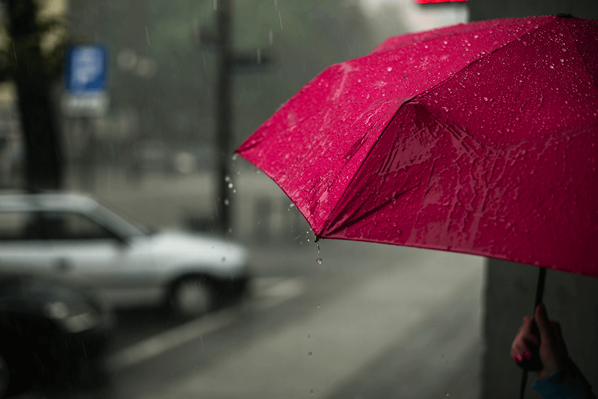 A woman holding a pink umbrella over her head on the sidewalk on a rainy day.