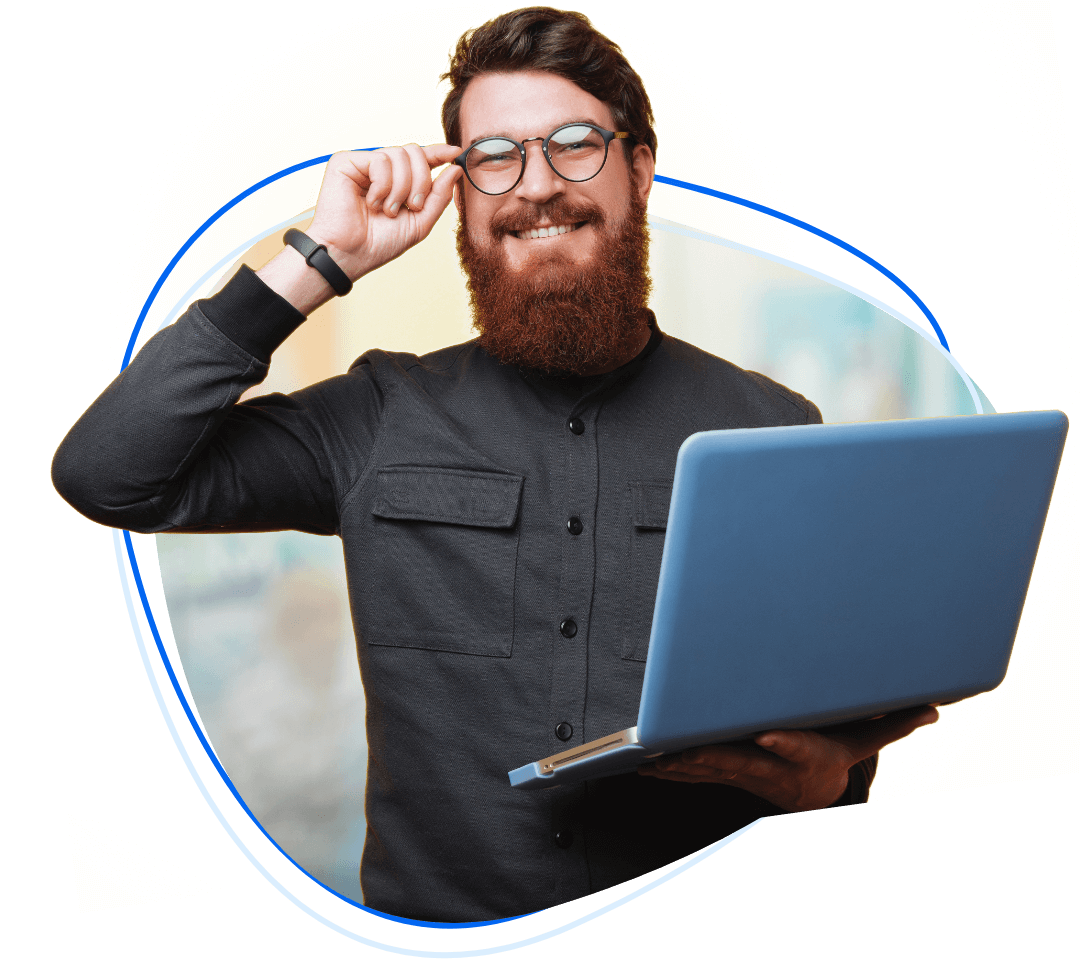 man with beard holding a computer touching his glasses.