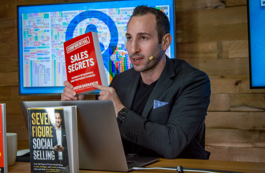 Brandon Bornancin holding up his Sales Secrets book while giving a presentation