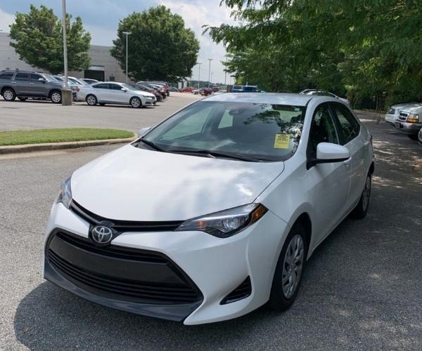 A white Toyota Corolla in an Tree lined Parking lot