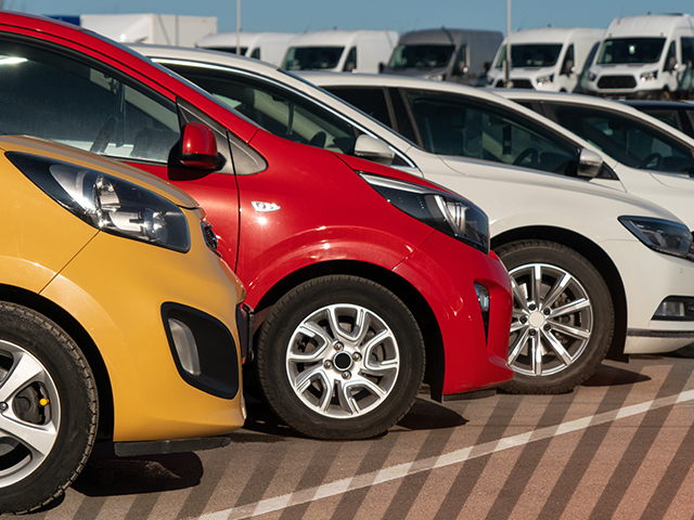 A row of cars with different colors in a parking lot ranging from yellow, red and white.