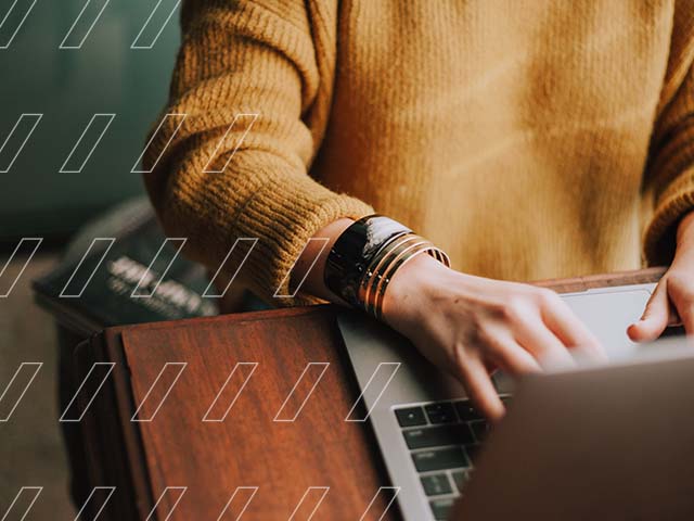 A women with a yellow sweater searches information on her laptop