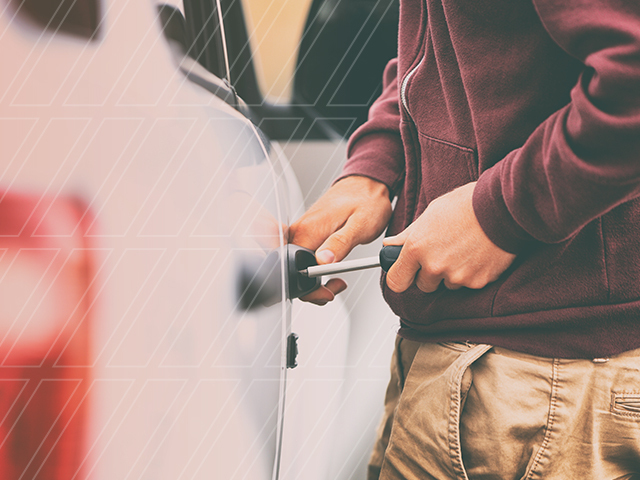 A man with a maroon hoodie trying to use a screwdriver to open a car door