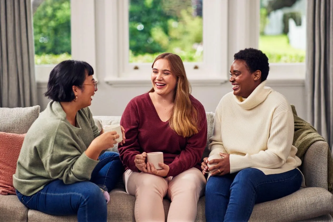 Three women sitting on a couch having a conversation over a cup of coffee