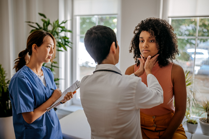 medical provider examining a patient's thyroid with a nurse taking notes