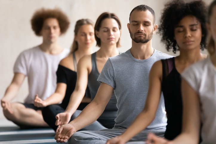 Group of diverse people meditating together visualizing during yoga morning session, seated cross-legged in a row