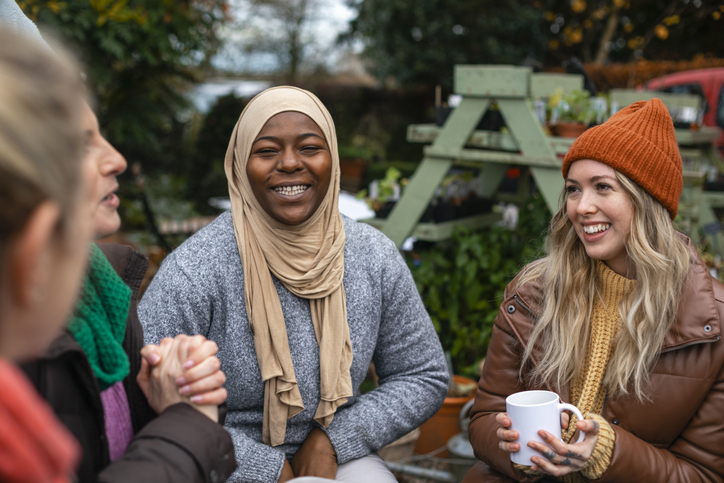 Volunteers sitting outdoors wearing warm casual clothing on a sunny cold winters day. They are resting and having a tea break from working on a community farm, looking after crops and performing other sustainable and environmentally friendly tasks. They are laughing and talking together, drinking hot drinks.