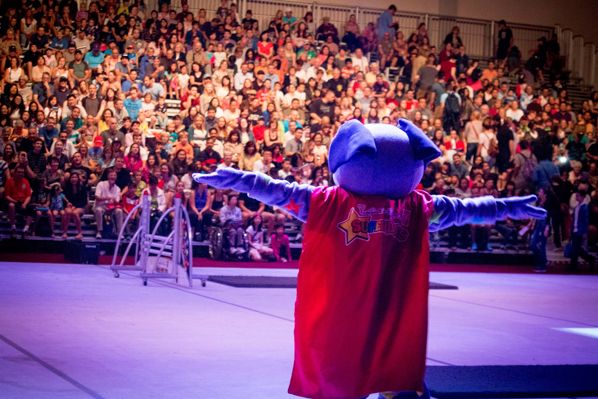 A mascot with a red cape performs for a crowd.