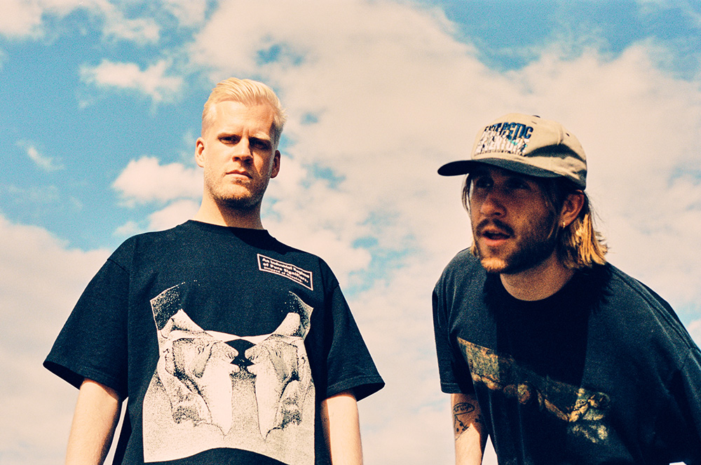 Oliver Lee and James Carter of Snakehips pose for a photo with a cloudy sky in the background.