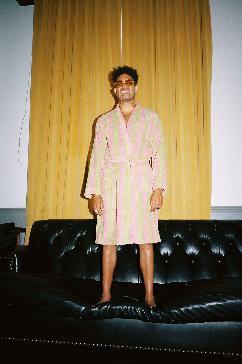 Bryce Vine stands on a black couch while wearing a robe.