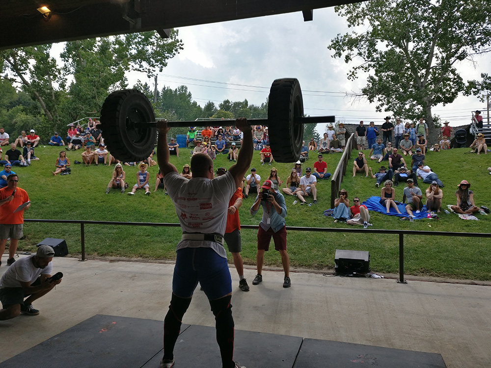 A man lifts a heavy barbell over his head on stage during a strongman competition.