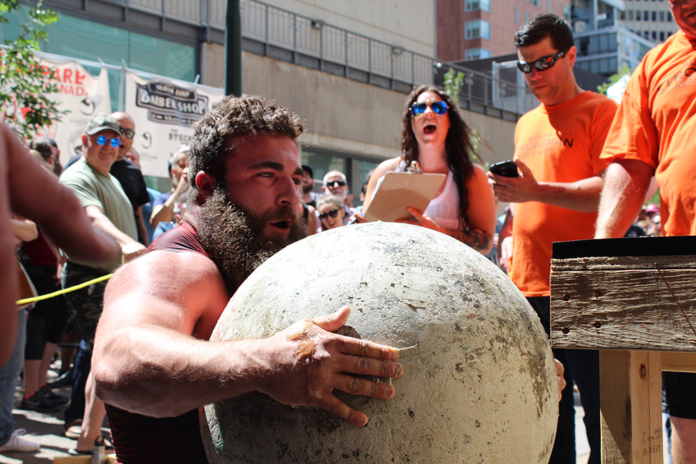 A man lifts an Atlas stone during a strongman competition.