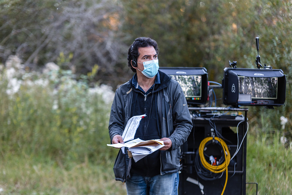 A film director flips through script papers while on an outdoor film set.