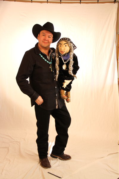 DerRic Starlight wearing a cowboy hat stands holding one of the puppets from his show