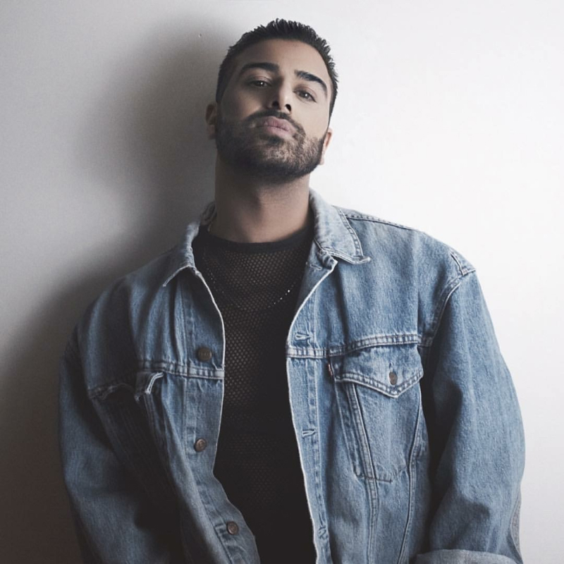 Khaled Rahime leans against a white wall wearing a denim jacket