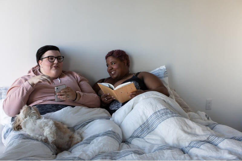 women reading and one holding mobile phone in bed