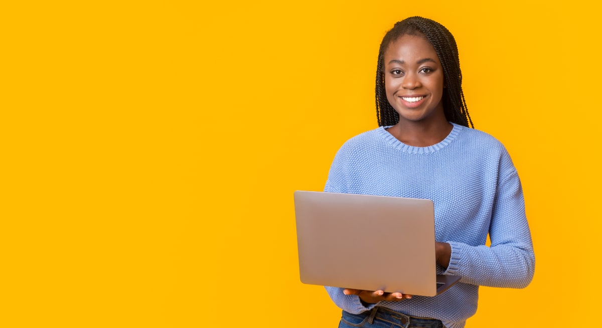 Woman on laptop smiling against a bright yellow background