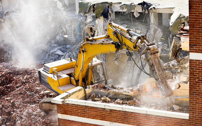 yellow excavator with a hydraulic breaker on a residential demolition site