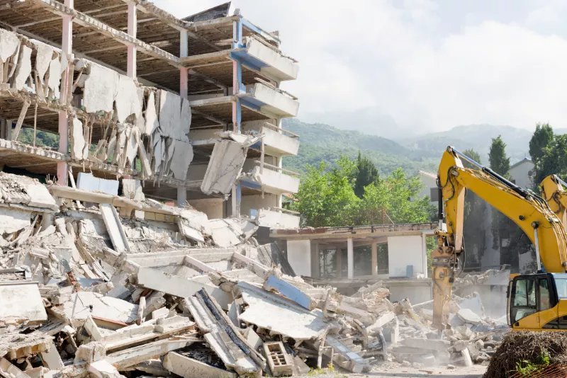 yellow excavator with hydraulic breaker attachment being used on site to break down a block of flats