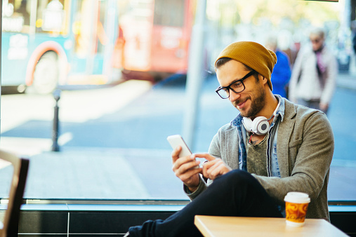 Hipster guy checks smartphone in coffee shop