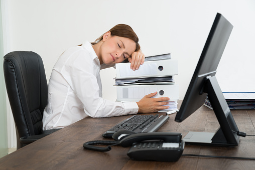 Woman sleeping on stack of binders at her desk