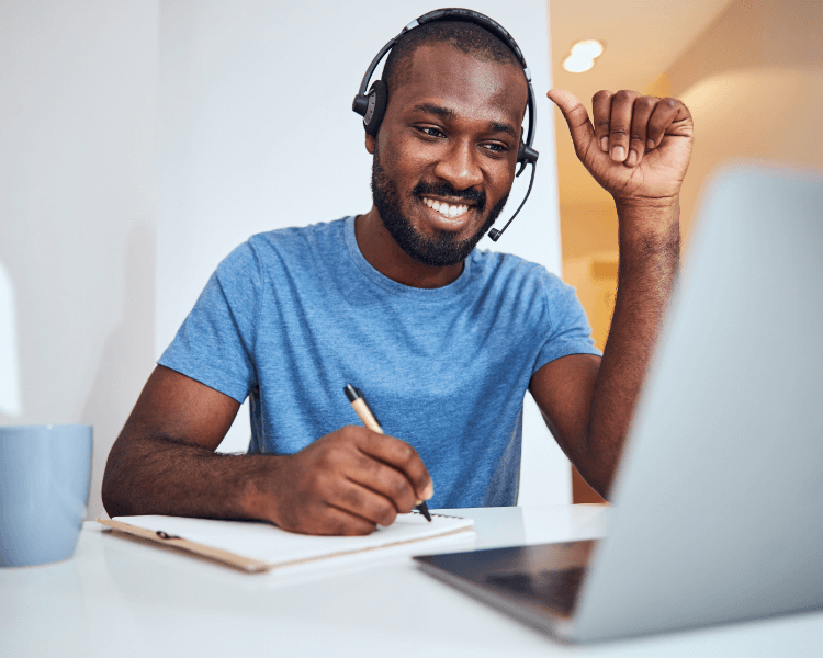 Man wearing a headset taking notes in front of a laptop.