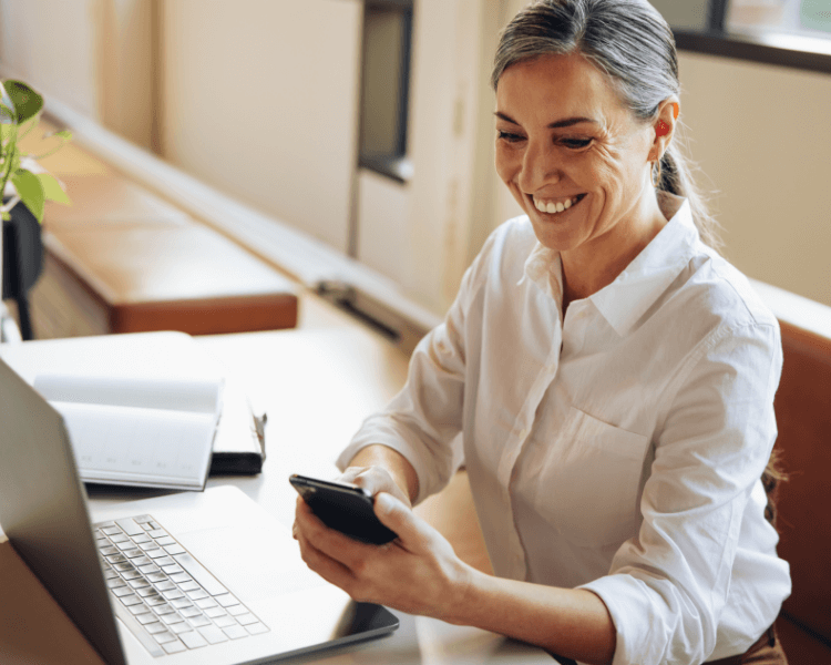 A woman using her phone in front of a laptop.