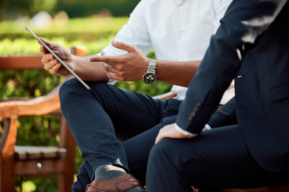 Zoomed in photo of 2 businessmen discussing something on a tablet while sitting outside on a bench