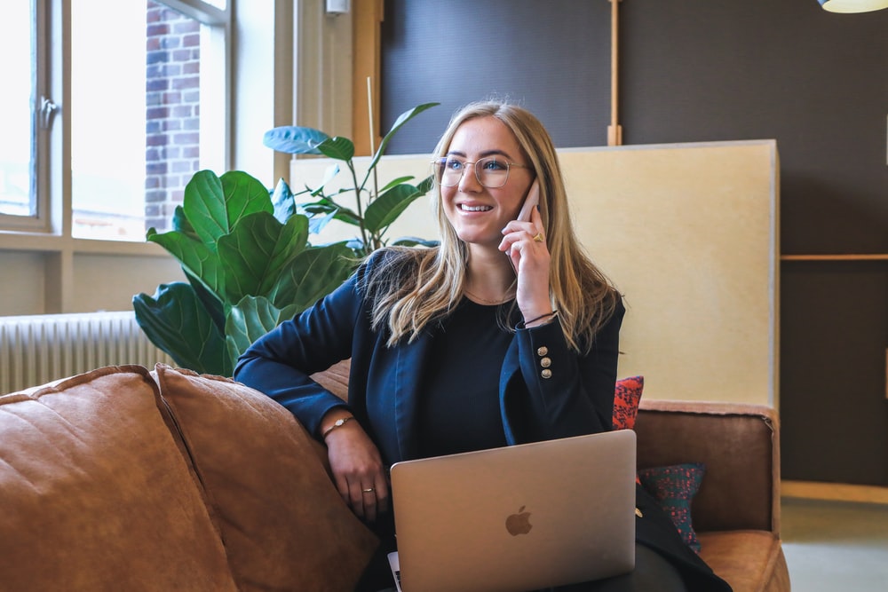 a business woman on her phone while sitting on a couch with a laptop.