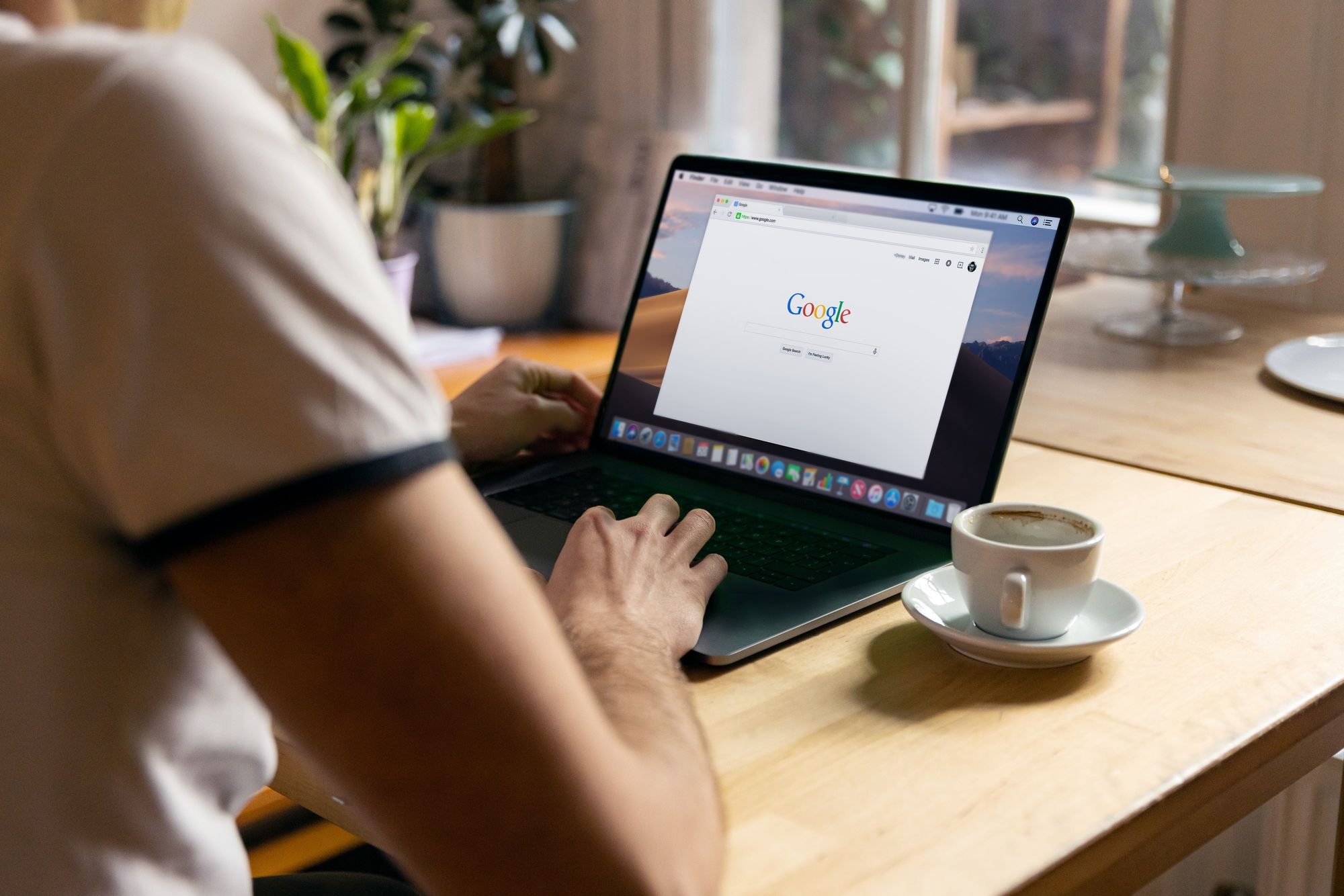 A close up photo of a person on a laptop browsing Google while having a coffee.