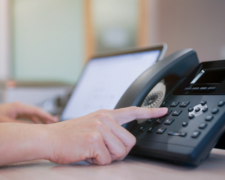 A hand dialing on a landline phone system