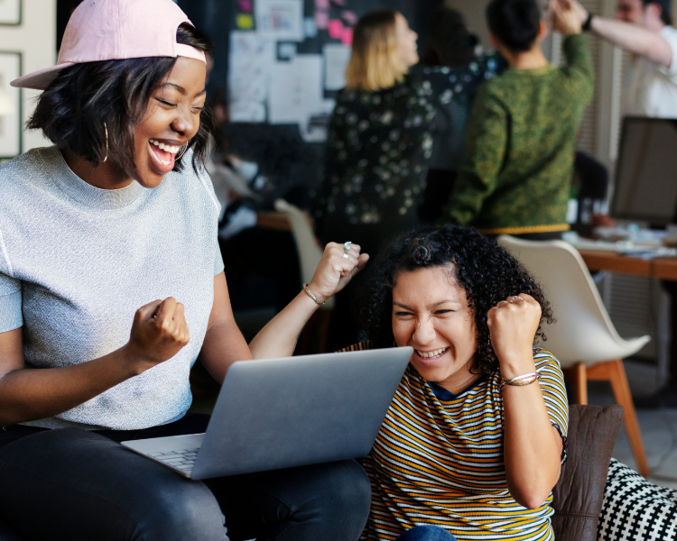 Two women cheering, the woman on the left has a laptop