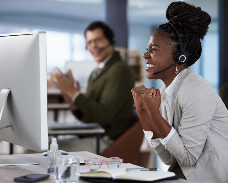 Woman with headset on celebrating in front of her computer