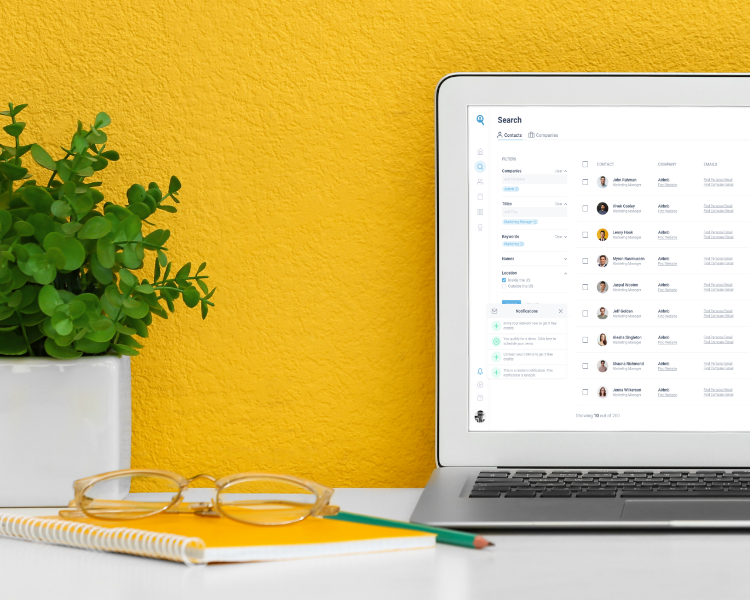 A laptop with Seamless.AI on the screen on a desk with a plant with a bright colored wall.