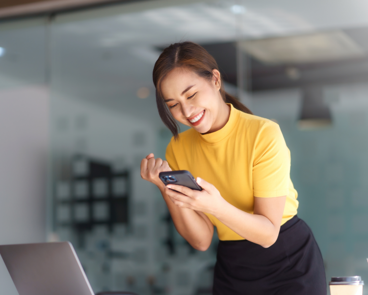 A smiling woman looking at her phone in celebration.