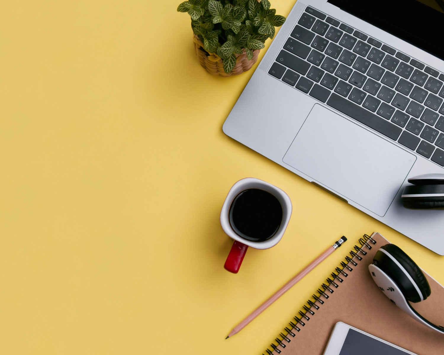 Desk with a laptop, coffee, notebook, plant, and pencil.