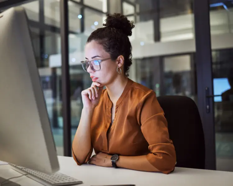 a woman sitting at a computer in the evening thinking about how to buy sales leads