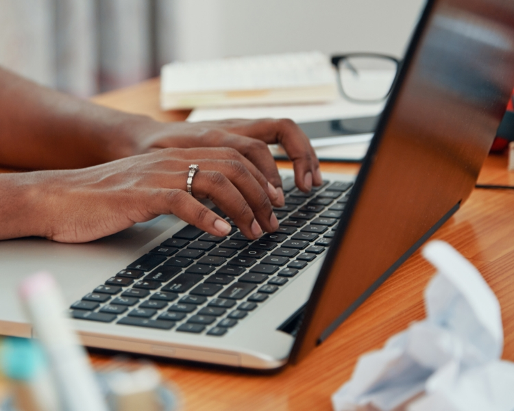 A person typing on a laptop writing for the sales team.