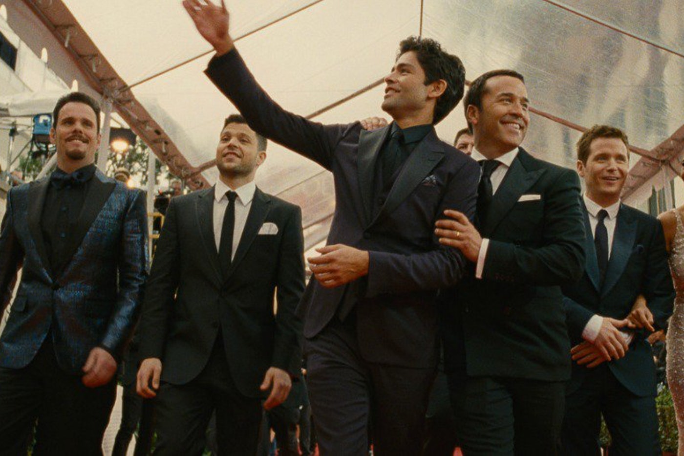 Movie still from Entourage. A group of men in suits smile and wave at a red carpet event.