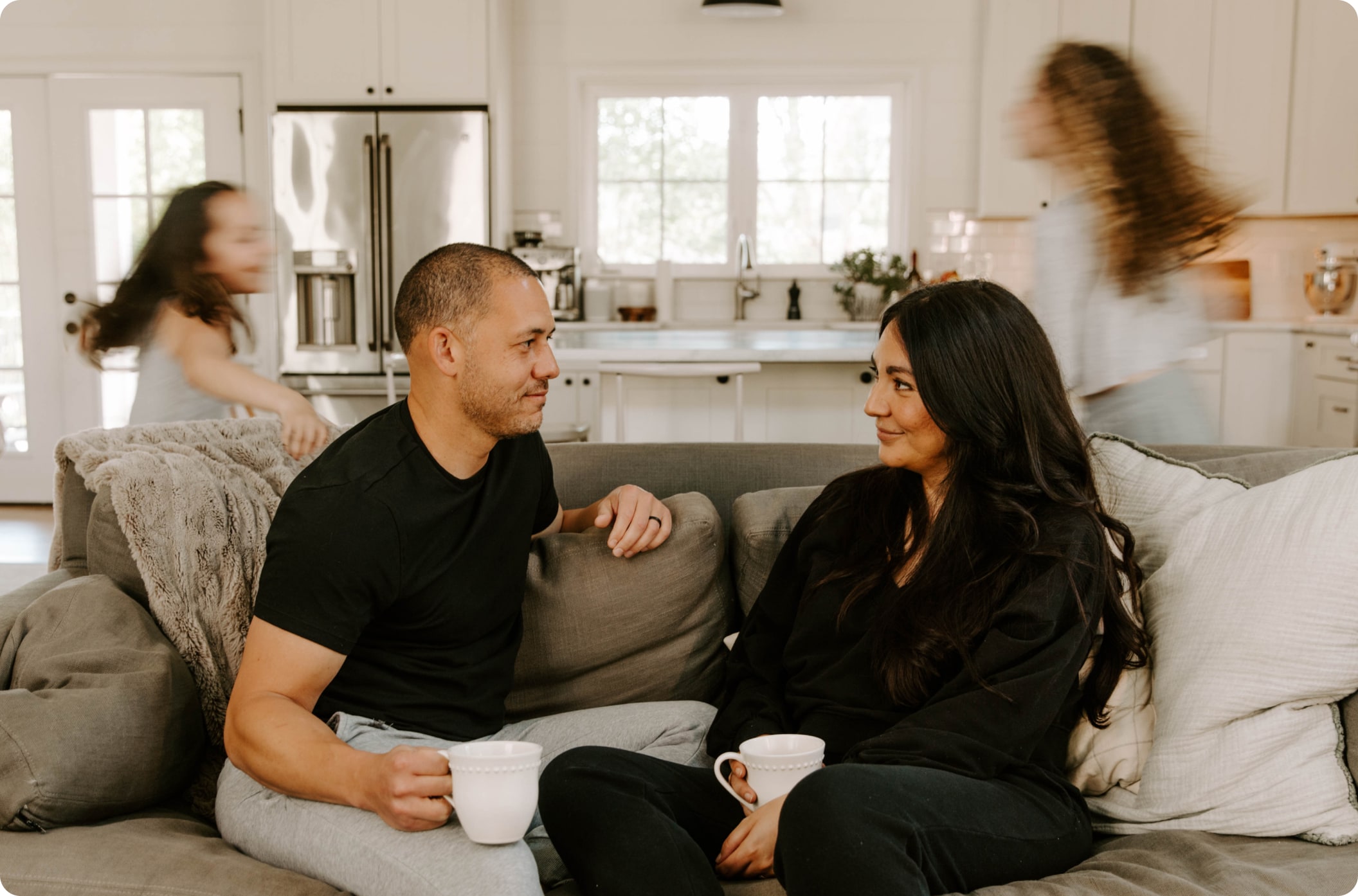 A family is gathered in the living room. Teenage kids run around while the parents relax on the sofa.