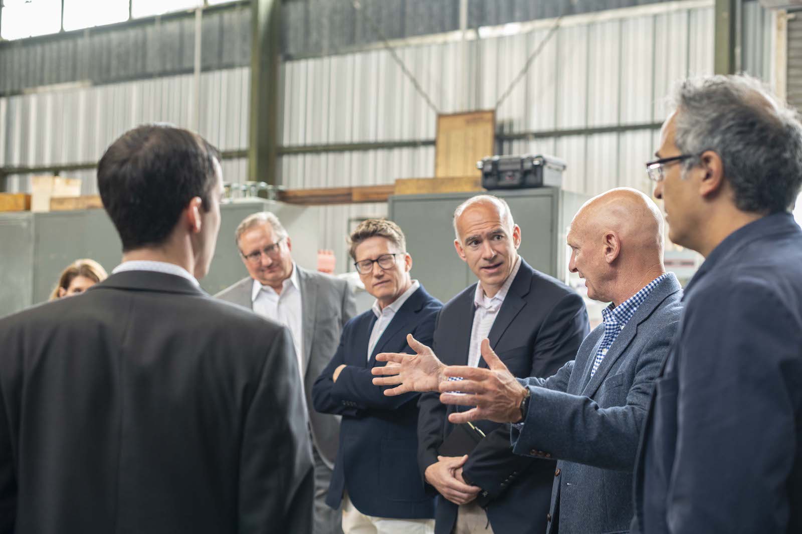 Side view of a group of about seven people all listening to one person talking and holding out his hands shoulder width apart