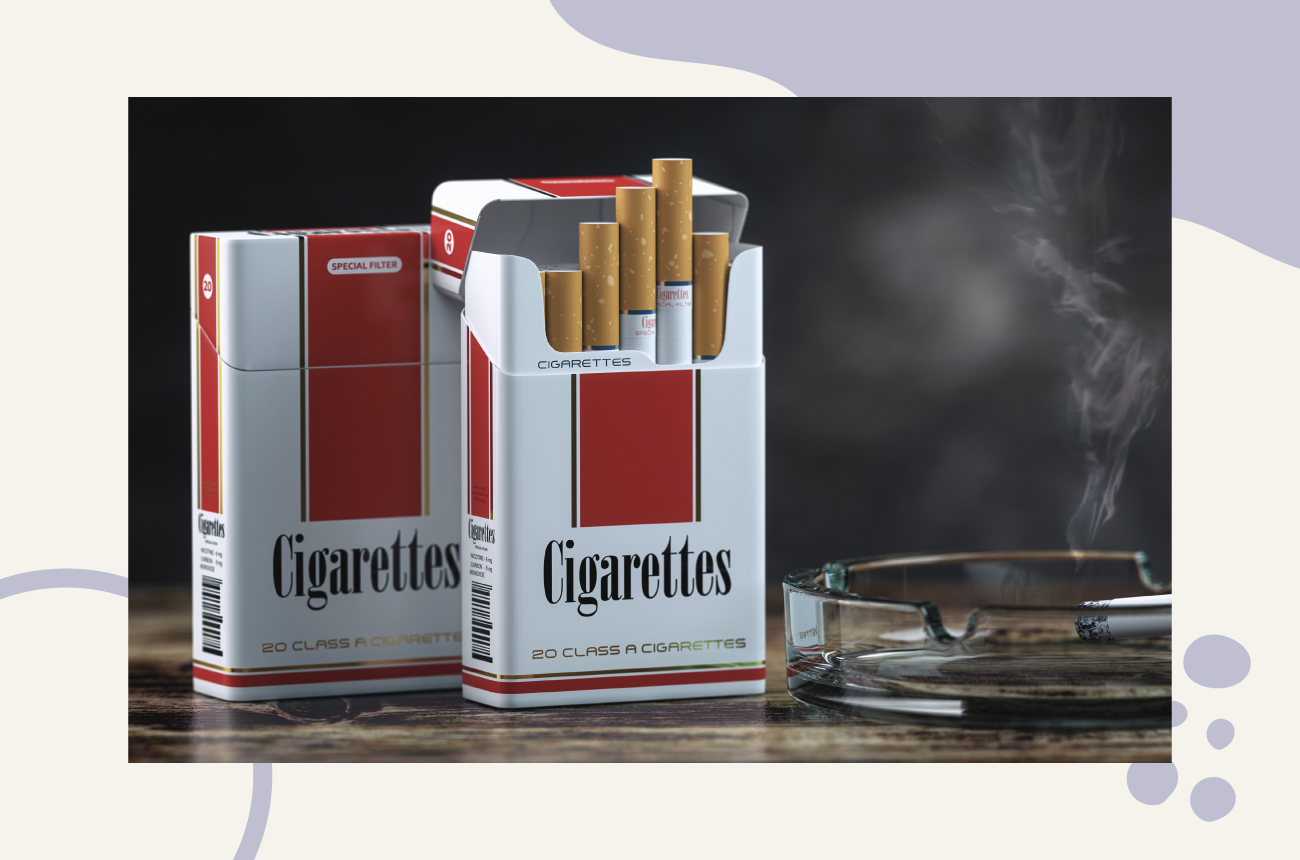 Cigarettes in a pack with a lit cigarette in an ash tray sitting next to them