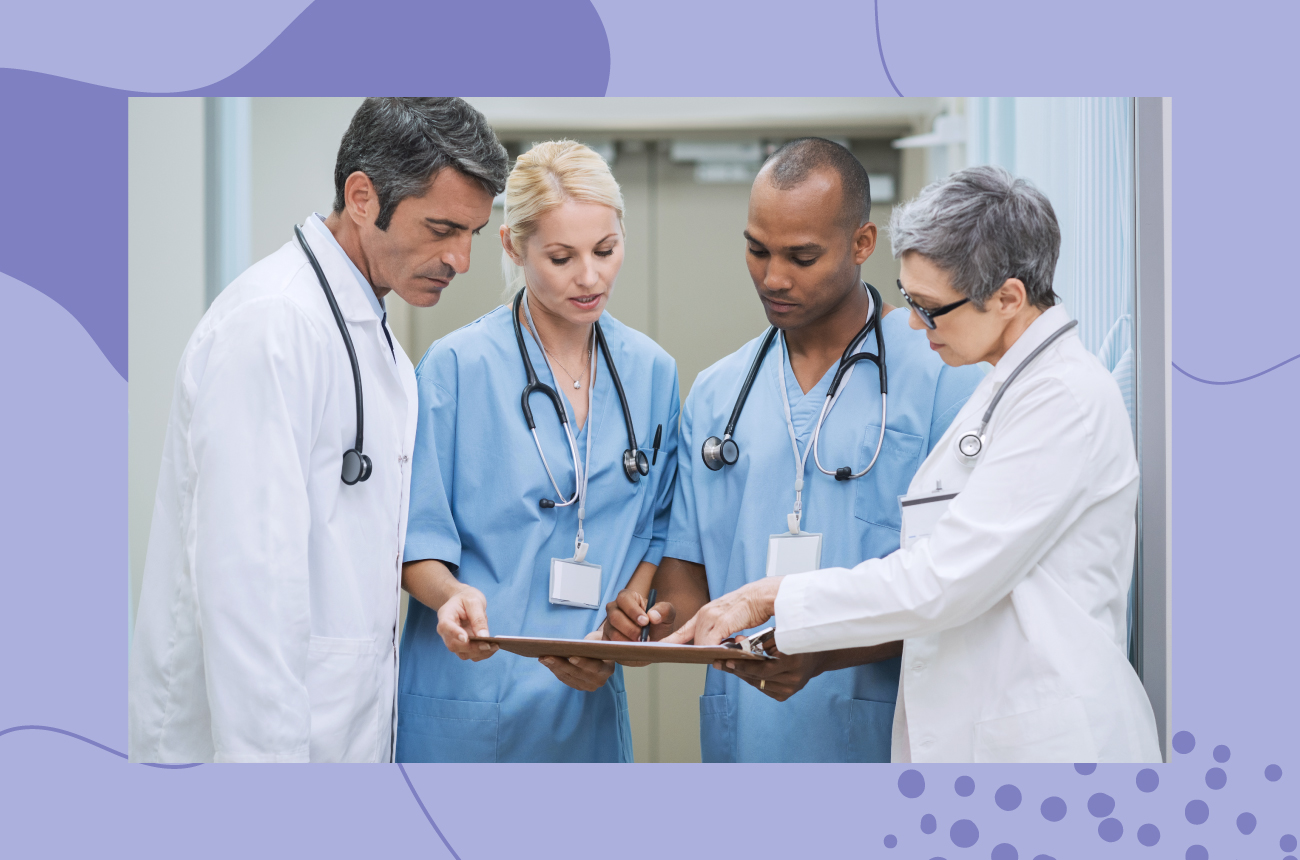Four male and female doctors standing in a group viewing and reading a patient chart