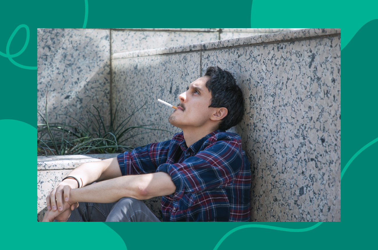 man sitting against wall smoking cigarette