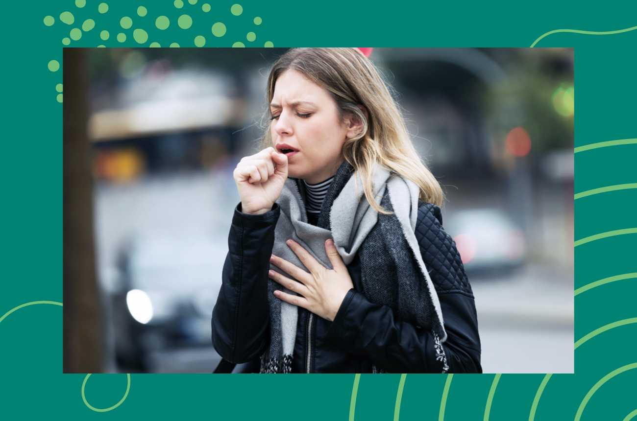 young blonde woman coughing into a closed fist while standing outside