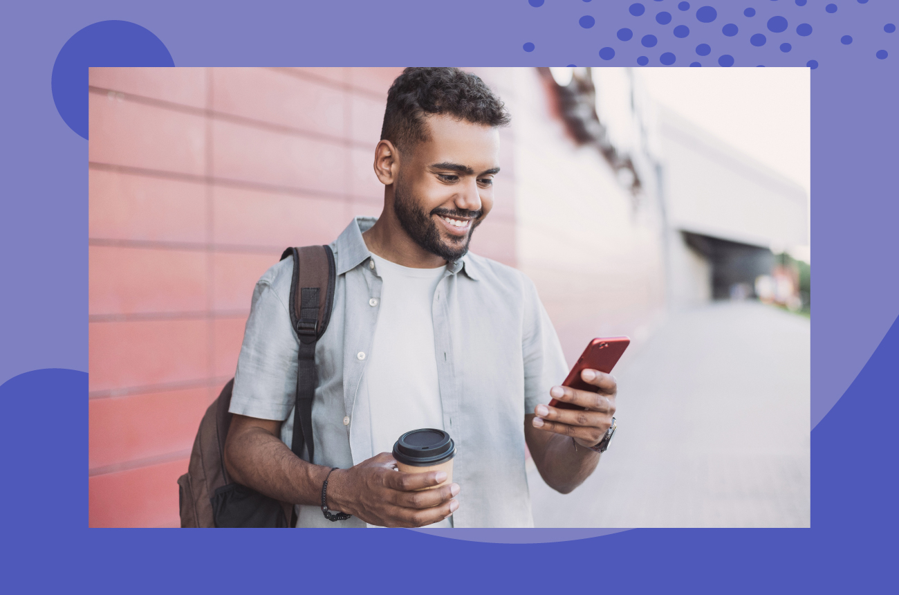 Young man holding a coffee in one hand and smiling while holding his phone in the other