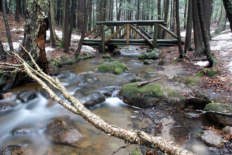 A partially frozen stream runs beneath a wooden bridge at Dippikill.