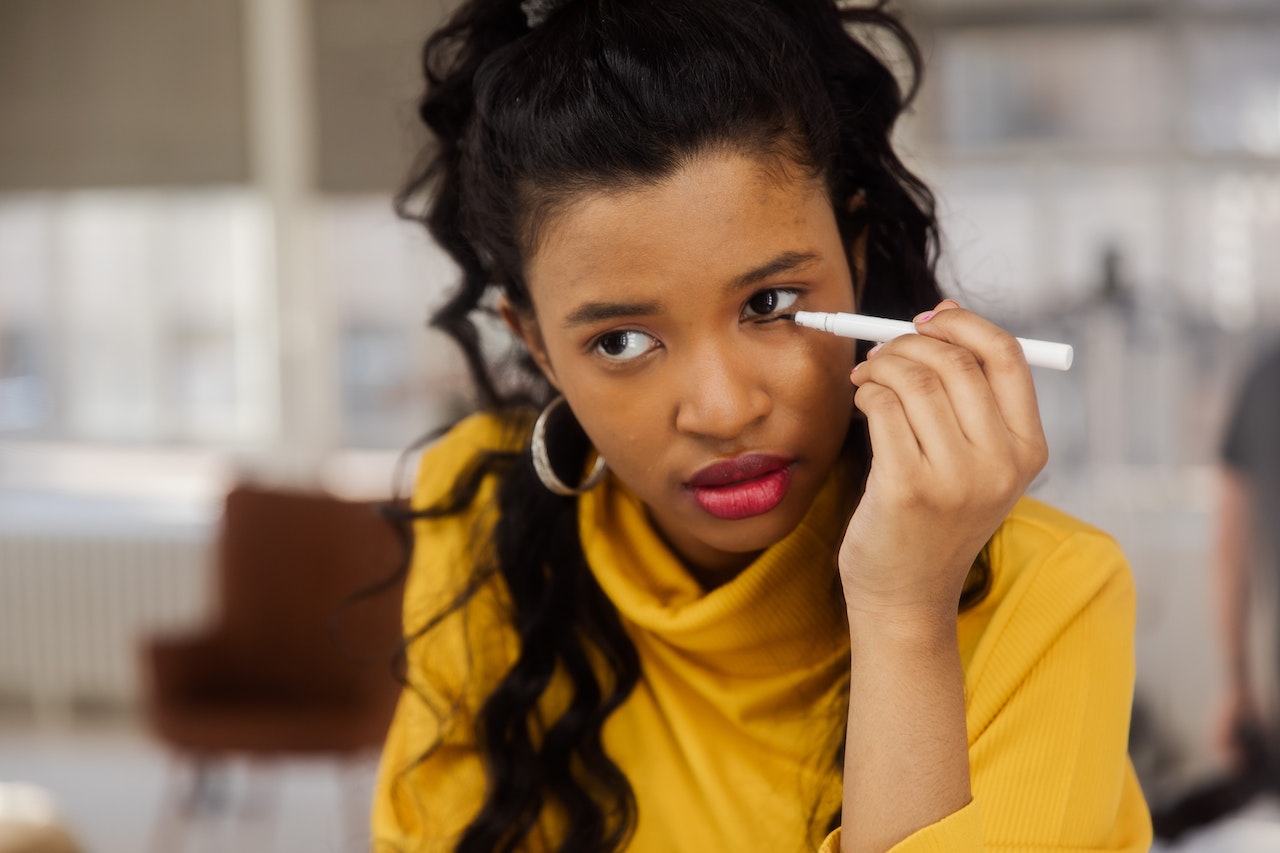 Woman in yellow turtleneck shirt putting eyeliner