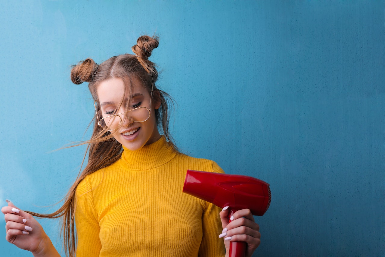 Woman in Yellow Sweater Using Red Hairdryer on Blue Background